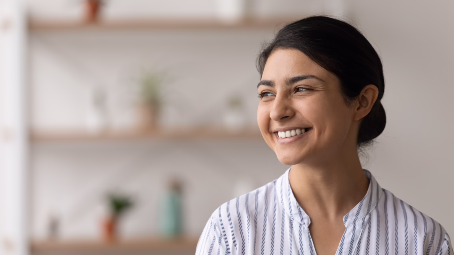 Close-up portrait of a smiling woman with dark hair in a striped blouse indoors in soft lighting
